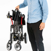 Man standing beside a folded Feather power wheelchair, holding it by the handle