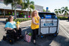 Woman in a power wheelchair and a companion beside a Harmar AL500 (base model shown) folded on the back of a black SUV