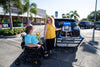 Companion unfolding a Harmar AL500 (base model shown) behind a black SUV while a woman in a power wheelchair waits
