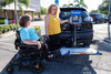 Harmar AL500 (base model shown) platform lowered behind an SUV next to a woman in a power wheelchair