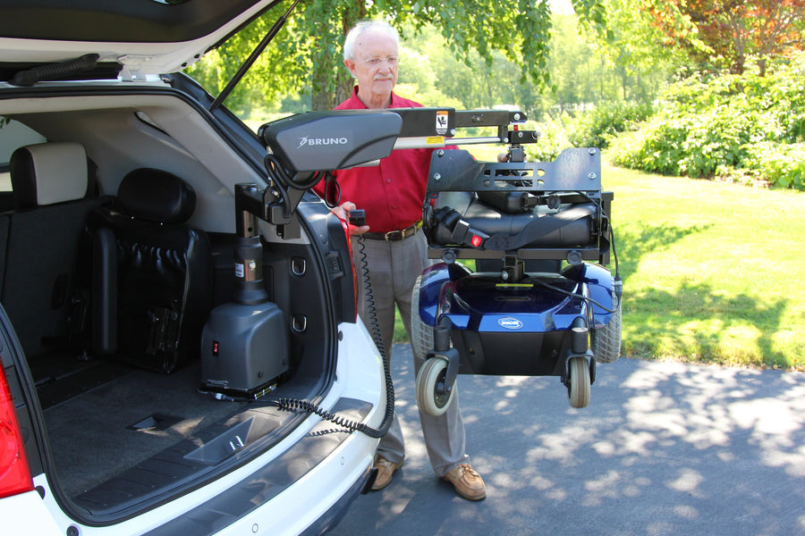 Man using a Bruno VSL-6900 Curb-Sider to lift a blue power wheelchair into the back of a white SUV