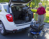 Bruno VSL-6900 Curb-Sider lowering a power wheelchair behind a white SUV as a man holds the hand control