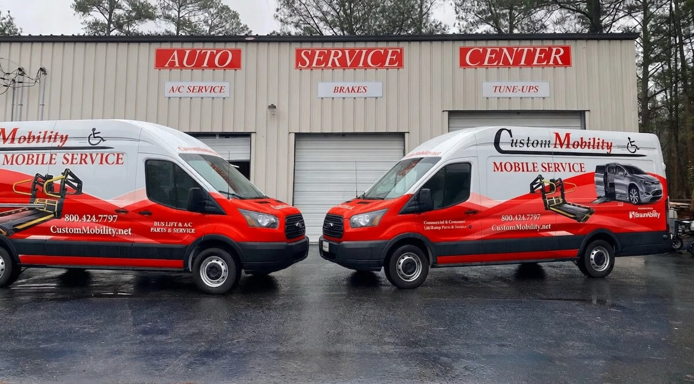Two red and black vans with 'Custom Mobility' branding in front of a service center.