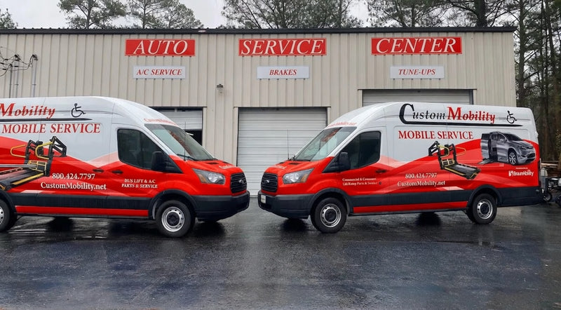 Two red and black vans with 'Custom Mobility' branding in front of a service center.