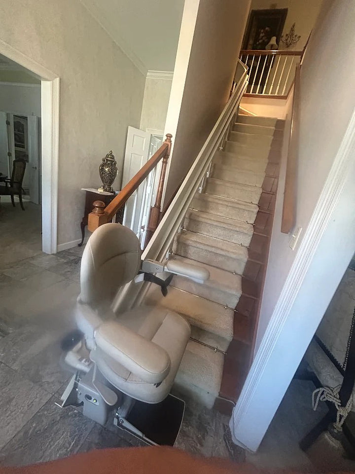 Bruno curved stairlift at the foot of carpeted stairs, rail rising along the wall