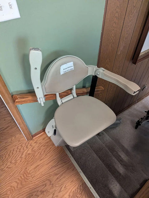 Bruno stairlift chair with arms raised at the top of carpeted stairs by wood panelling