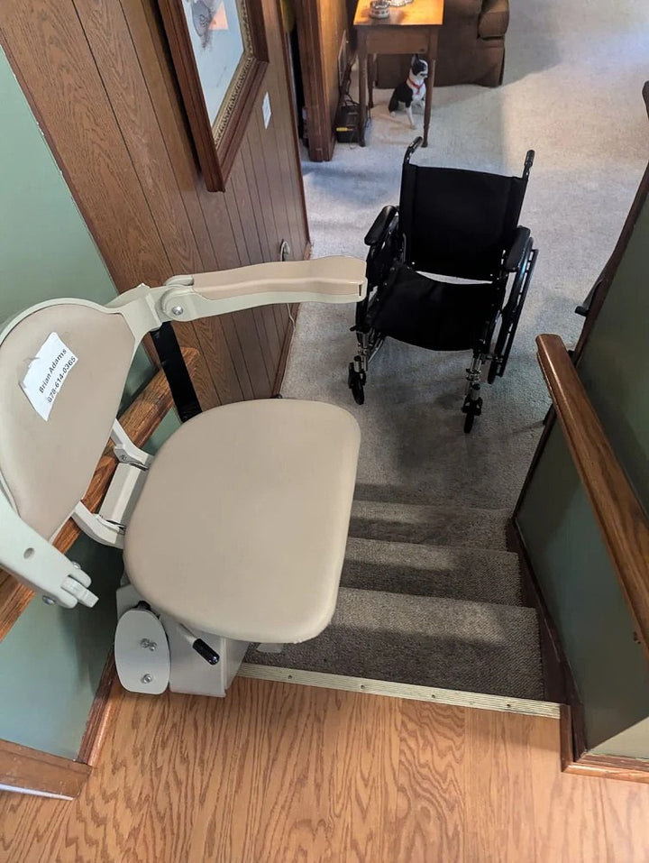 Bruno stairlift at the top of carpeted stairs, a wheelchair parked in the room beyond