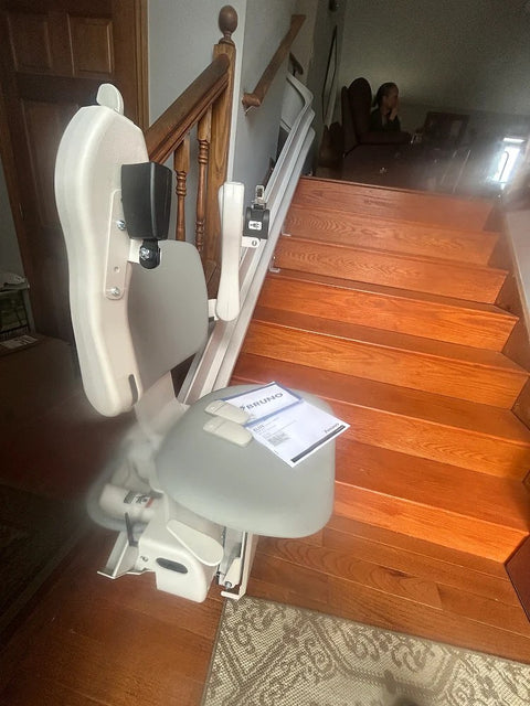 Bruno stairlift folded at the foot of wooden stairs, owner manual resting on the seat