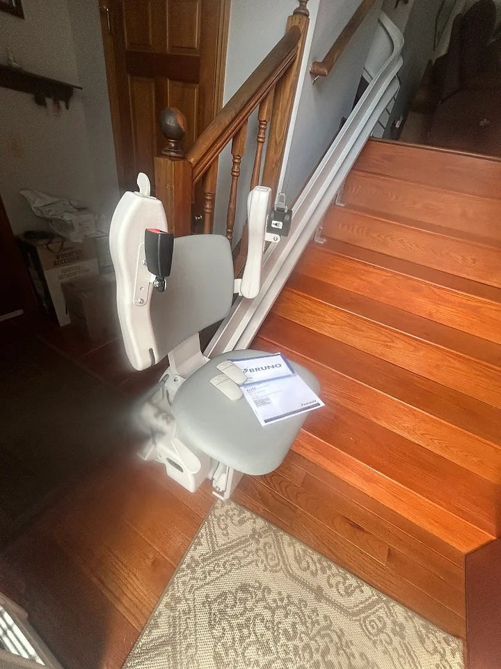Bruno stairlift at the bottom of a wooden staircase beside a patterned rug