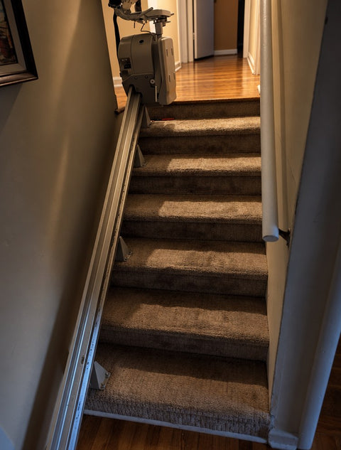 Bruno stairlift rail running up carpeted stairs with the chair parked at the top