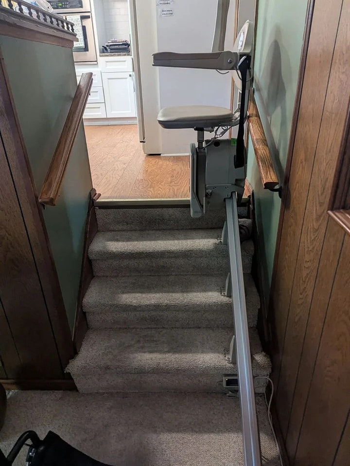 Bruno stairlift rail down carpeted stairs from a kitchen doorway, chair at the top
