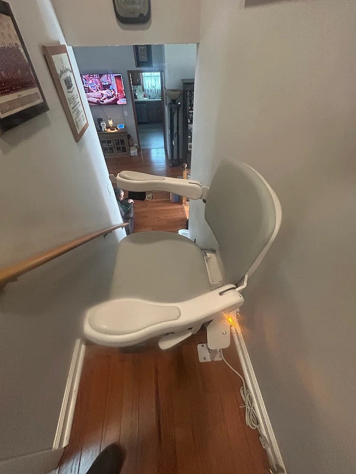Bruno stairlift parked at the top of stairs in a hallway, seat folded and arms raised