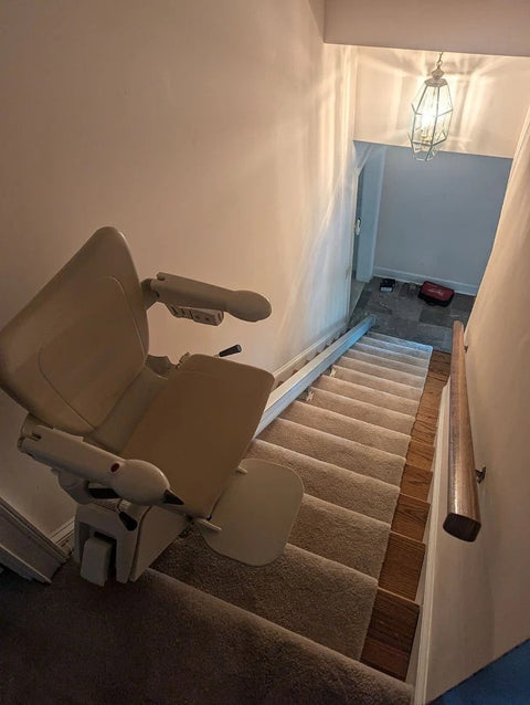 Handicare 1100 stairlift at the top of carpeted stairs leading down to a hallway