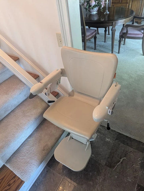 Handicare 1100 stairlift with arms down at the foot of stairs by a dining room