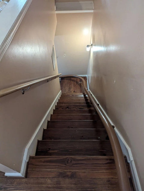 Handicare curved stairlift rail in brown curving down a narrow wooden staircase