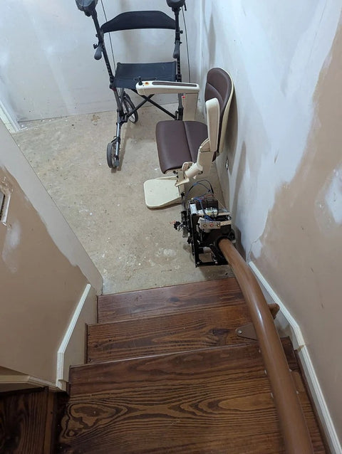 Handicare curved stairlift at the top of wooden stairs, a rollator on the landing