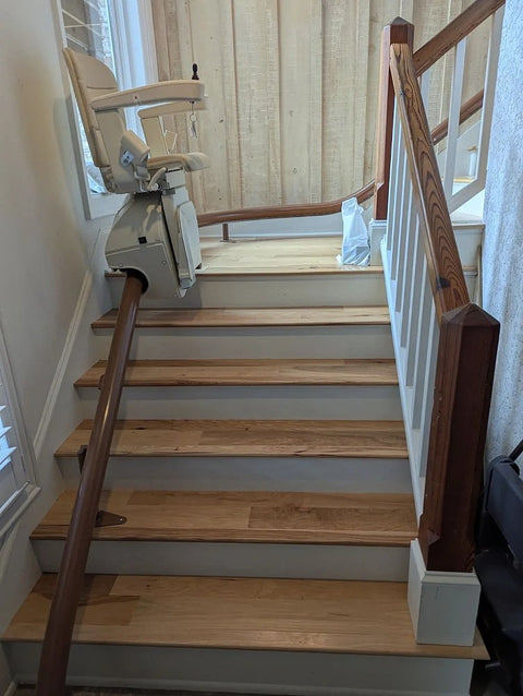 Handicare stairlift rail up light wooden stairs to a landing with a white banister