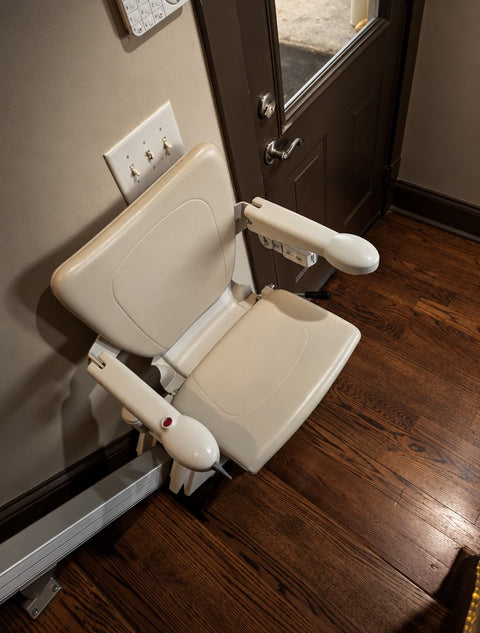 Handicare stairlift chair with arms folded down beside a back door, on a wooden floor