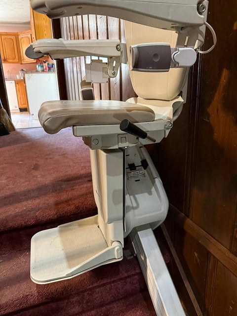 Handicare stairlift chair with footrest down at the foot of stairs by wood panelling