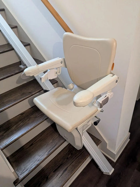 Handicare stairlift with arms down at the foot of dark wooden stairs