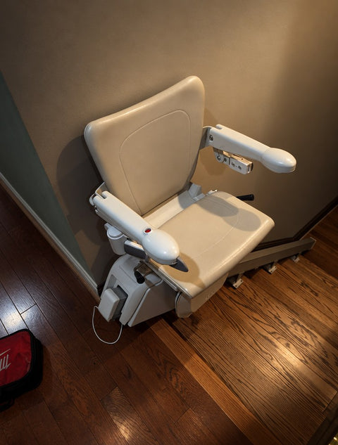 Handicare straight stairlift at the foot of wooden stairs with the seat and footrest folded down