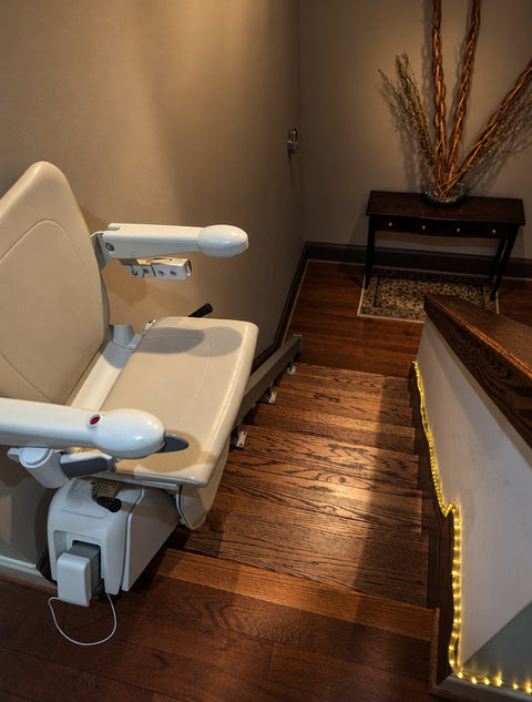 Handicare straight stairlift parked at the bottom of a wooden staircase beside a small hall table