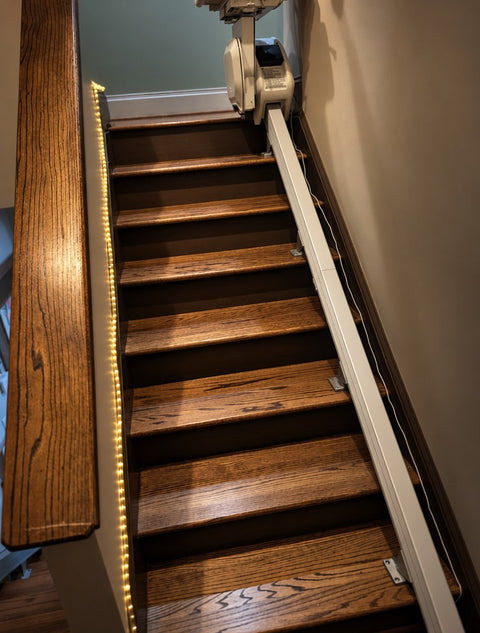 Handicare stairlift rail running up wooden stairs with a light strip along the step edges