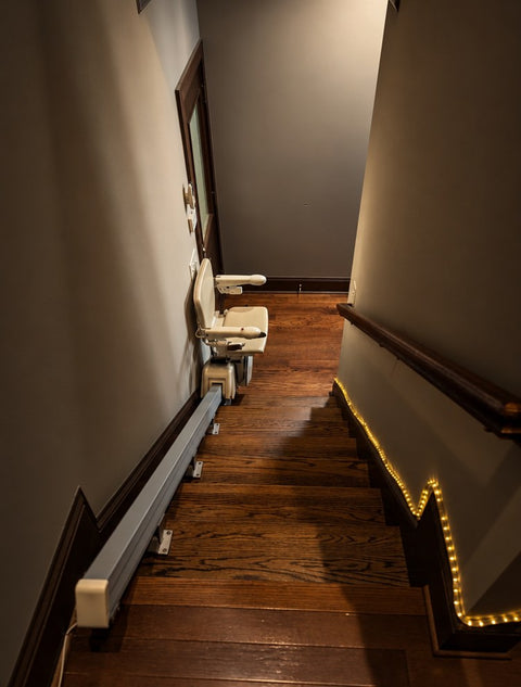 Handicare stairlift rail along a wooden staircase, seen from the top landing with the chair at the bottom
