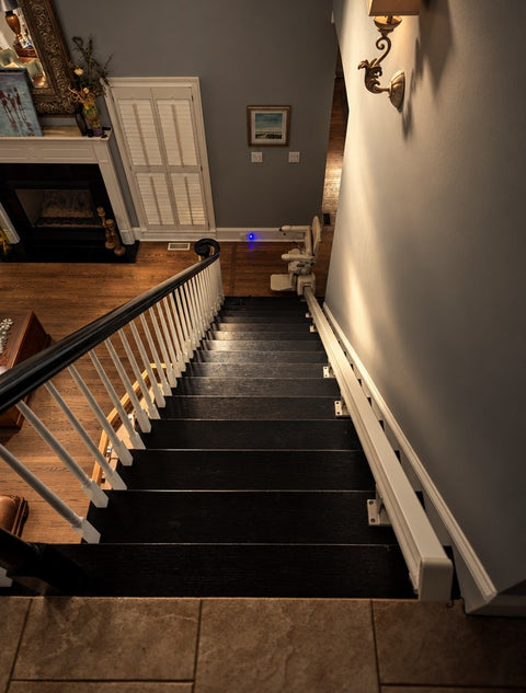 Handicare stairlift rail down dark wooden stairs into a living room with a fireplace