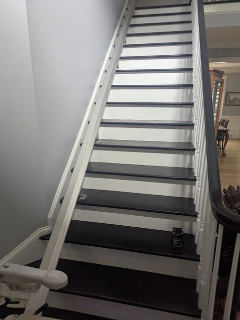 Handicare stairlift rail on a long staircase with white risers and dark treads