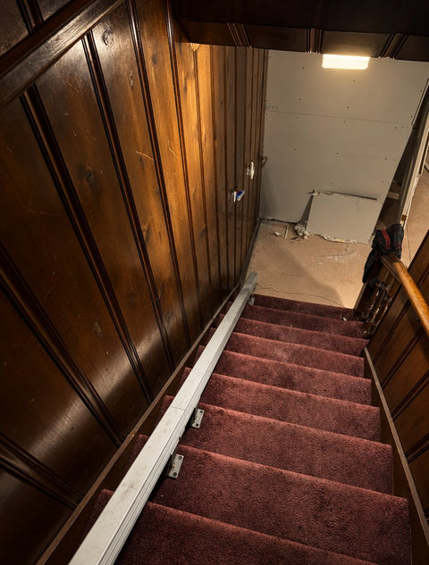 Handicare stairlift rail down pink carpeted stairs beside dark wood panelling