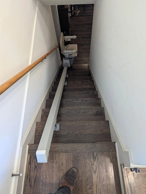 Handicare stairlift rail down dark wooden stairs, chair parked at the bottom