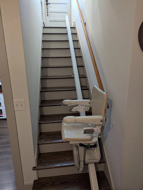 Handicare stairlift on a white rail at the top of stairs with dark treads