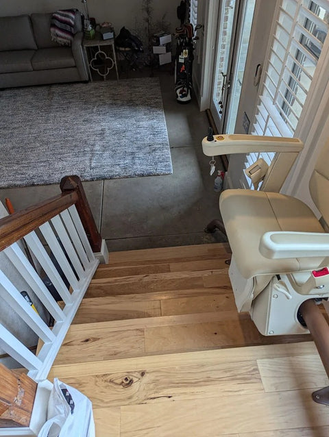 Handicare stairlift parked at the top of light wooden stairs above a living room