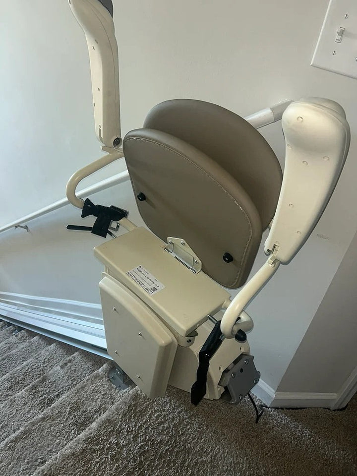 Harmar stairlift folded at the foot of carpeted stairs beside a light switch