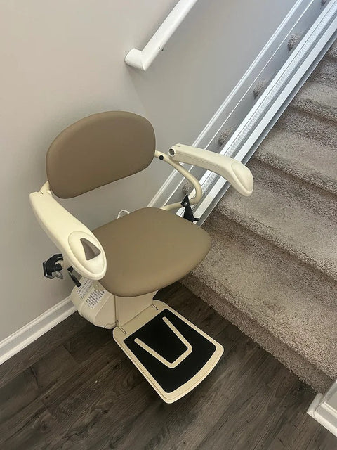 Harmar stairlift with a taupe seat and footrest down at the bottom of carpeted stairs