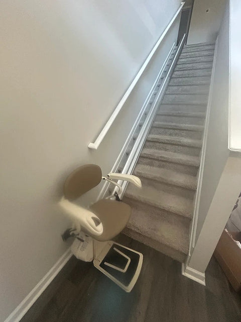 Harmar stairlift at the foot of a long carpeted staircase with its rail rising to the top