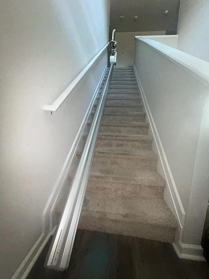 Harmar stairlift rail running up a long carpeted staircase beside a white handrail