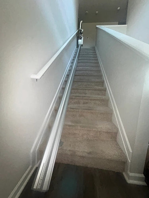 Harmar stairlift rail running up a long carpeted staircase beside a white handrail