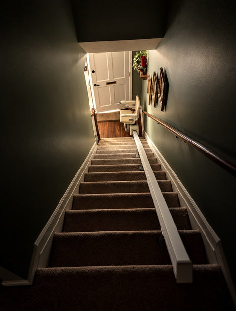 Stairlift rail running down carpeted stairs in a dark-walled stairwell toward a front door