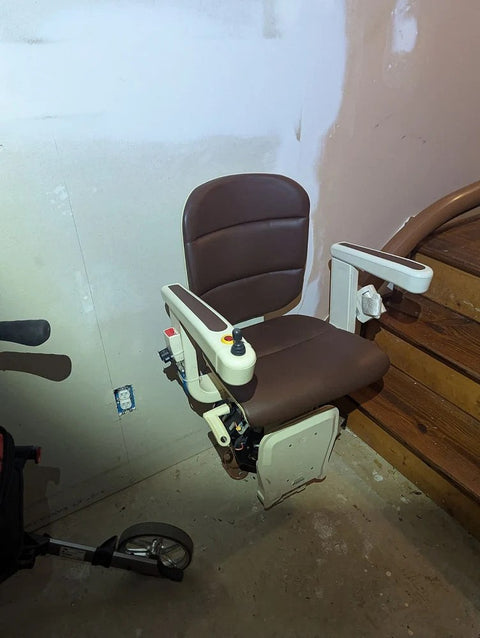 Handicare curved stairlift chair on its rail during a repair, brown seat and armrests