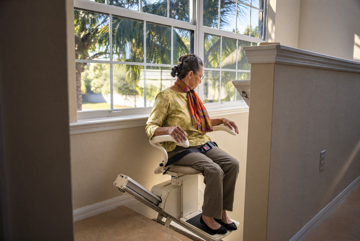 Woman in a scarf seated on a Harmar Pinnacle SL300 stairlift at the top of the stairs, beside a large window